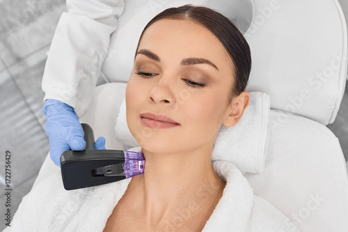 Close-up of radiofrequency neck lift procedure on pretty woman to tighten and improve condition of her skin. RF lifting