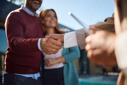 Close up of couple shaking hands with real estate agent while buying new home.
