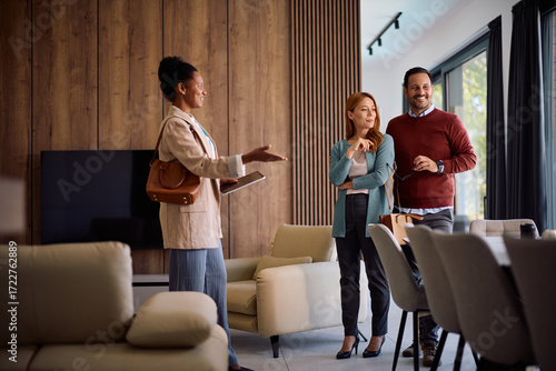 Black real estate agent showing new house to happy couple during open house day.