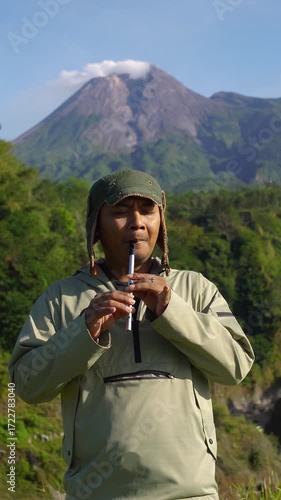 A male musician plays a traditional Irish instrument called a tin whistle against the backdrop of an active volcano. A tin whistle player shows off his skills in the wilderness on a sunny morning.