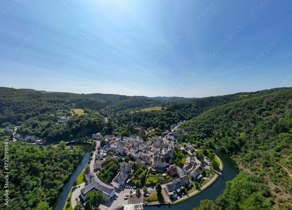 Fototapeta premium Esch-sur-Sure, Wiltz, Grand-Duche de Luxembourg, August 10, 2025, This stunning aerial view captures a picturesque village perfectly nestled amidst scenic hills and a winding river