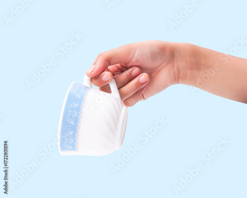 Female hand holding elegant white and blue patterned cup on light blue