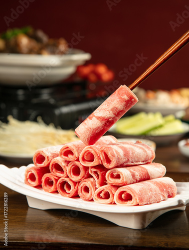 Raw lamb meat rolls with chopsticks for hot pot shabu shabu Asian cooking ingredients on white plate
