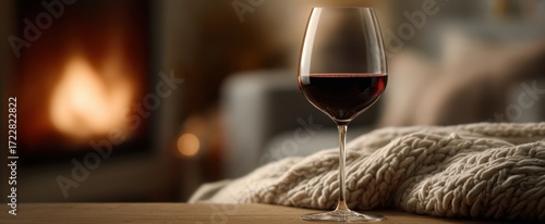 The elegant red wine glass beside a cozy blanket by the fireplace.
