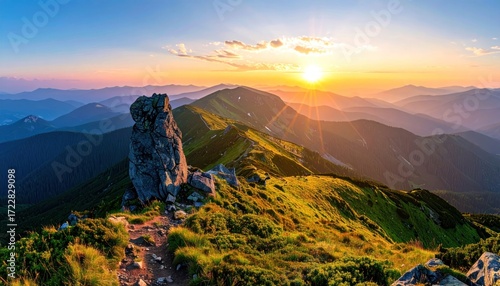 Stunning mountain vista during sunset, with a rocky pinnacle on a grassy ridge overlooking layered peaks illuminated by warm sunlight