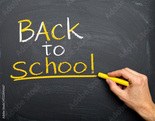'Back to school' written in white and yellow chalk on a dark blackboard, with a hand underlining 