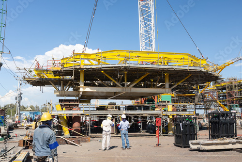 Offshore Platform Construction by crane lifting, erecting or install platform on structure, team of engineers and construction workers work together under blue sky, represent safety and precision.