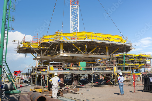 Construction offshore platform. Crawler crane lifting steel frame structure. Workers coordinate assembly, represent marine engineering, industrial construction, offshore energy technology.