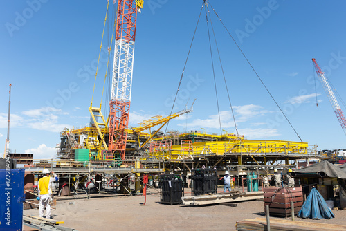 Heavy lifting with crane hoisting massive oil rig platform under clear blue sky. Showcases precision engineering and construction in natural gas, oil, and energy resources industry.