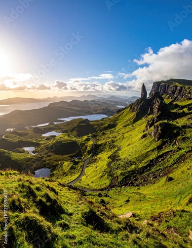Lush green mountainside with a winding road under a sunny, partly cloudy sky. Distant water features provide a serene backdrop