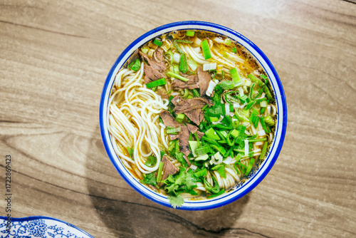 Close-up beef noodle with clear soup on wooden table, minced garlic, beef slices