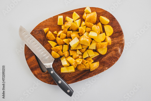 chopped baby potatoes on wooden board with knife on kitchen bench