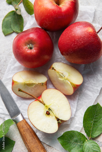 Freshly cut red apples on baking paper with knife and leaves