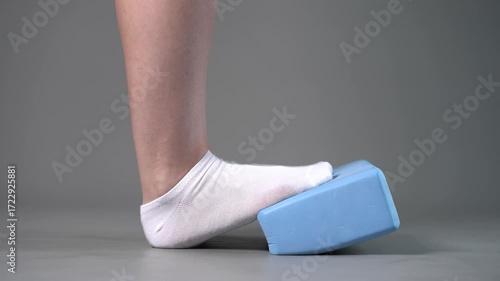 Individual balance training on a blue block with bare feet, demonstrating foot position and stability on a gray studio background