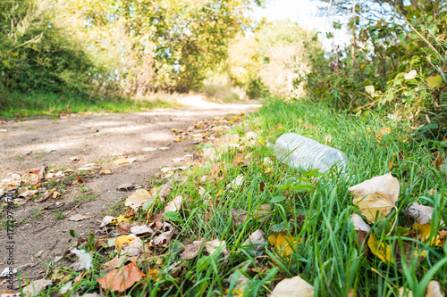 Illegally dumped plastic empty water bottle seen laying on a grassing embankment next to a footpath in a nature reserve in the UK. Only a few metres away is a litter bin which was not used.