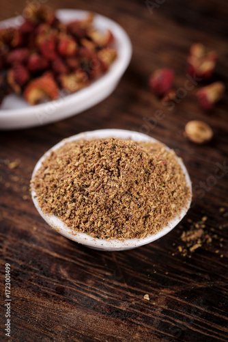 Ground Spice Powder in Bowl with Whole Spices on Rustic Wood Background