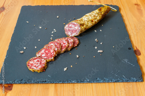 Salami sausages with spices on black slate board on a wooden table