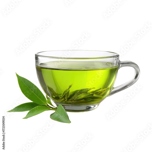 Transparent glass teacup filled with light green tea, with fresh green tea leaves beside it