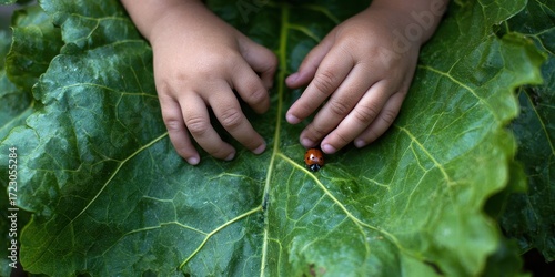 Wallpaper Mural Gentle Hands Meet Nature's Jewel: A child's tiny hands delicately cradle a vibrant green leaf, upon which rests a tiny ladybug. A perfect illustration of care and wonder. Torontodigital.ca