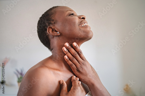 Smiling mature woman applying moisturizer on her neck