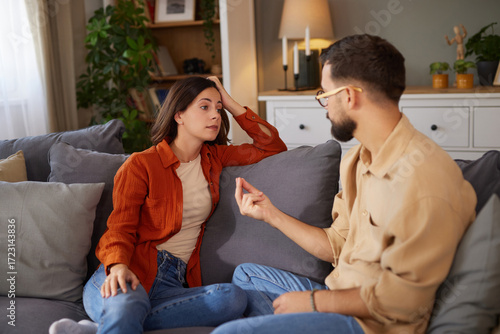 Two people have a serious conversation about their relationship while sitting together on a couch in a comfortable living room. The mood is tense as they share their feelings.
