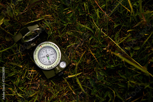 Green metal compass lying on the grass, concept of tourist equipment, finding the right direction of the path.