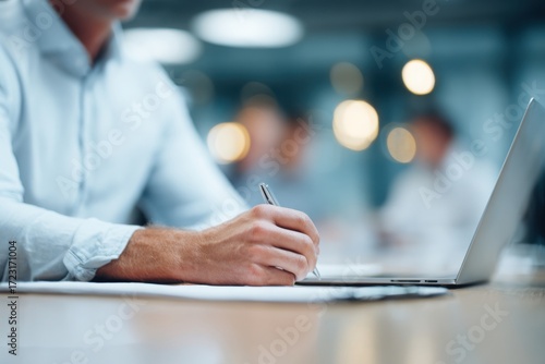 a businessman in a shirt is working on a laptop computer he taking notes or participating in a meeting in a conference room, using the laptop for a financial concept. the background is blurred.