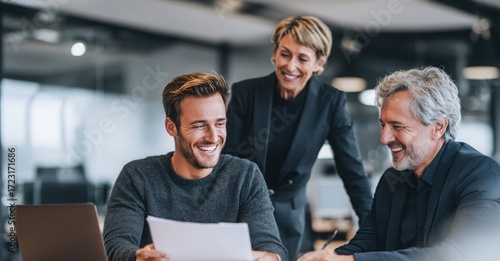 Group of professional colleagues smiling and discussing documents together at a desk during a business meeting in a bright office.