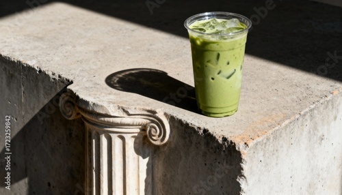 Iced matcha latte with ice in a clear plastic cup on a stone ledge with sunlight and shadow