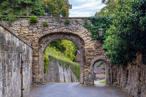Two Ancient Stone Arches Covered In Ivy And Weathered Brick Create A Narrow Inviting Alleyway Between Historic Walls