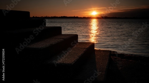 Serene sunset by a calm lake with golden reflections, concrete steps leading to water, peaceful atmosphere,
