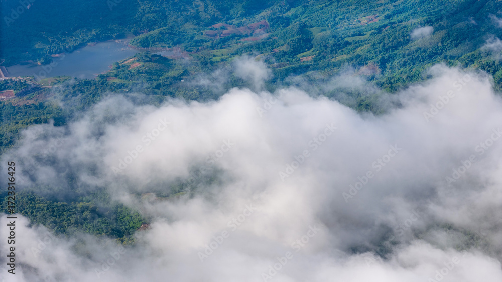 Obraz premium Aerial of Village in rain cloud cover tropical green mountain. Rainy season. Misty cover green forest. beautiful green village