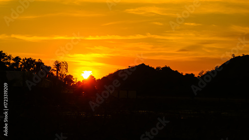 The sun sets behind the hills visible in silhouette