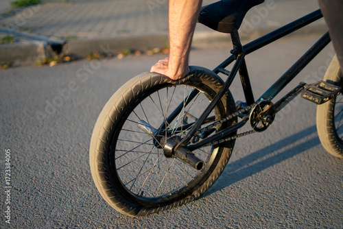 A BMX bicycle rests on a city street with a flat rear tire, highlighting the punctured condition under the warm light of sunset, surrounded by urban features.