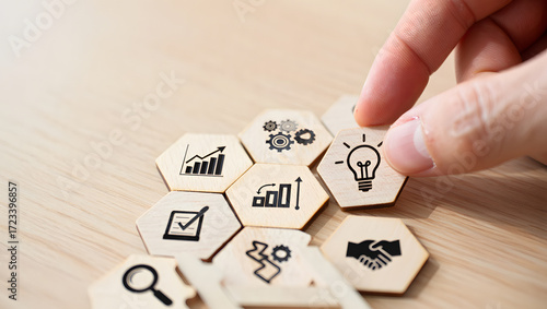 Hand placing a hexagonal tile with a lightbulb icon onto a cluster of business strategy icons
