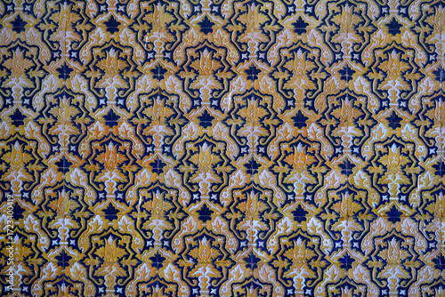 This is a detailed, close-up photo of traditional Sevillian azulejo tiles. The intricate pattern features a repeating design of yellow-orange 