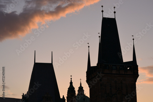 This is a silhouette shot of Prague's old town towers against a sunset sky. The photo highlights the distinct, jagged spires and rooftops of the city