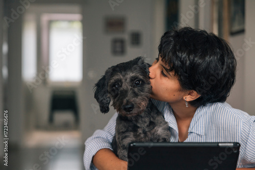 Young girl kissing her adorable dog while using the tablet at home