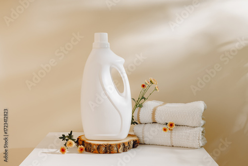 White mockup bottle of laundry detergent on wooden podium with towels and flowers with aesthetic shadows. Fabric softener with delicate aroma, laundry and washing concept