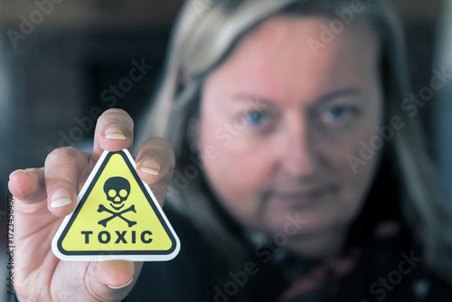Woman holding toxic warning sign, symbolizing toxic person, negative energy, harmful relationship, emotional danger.