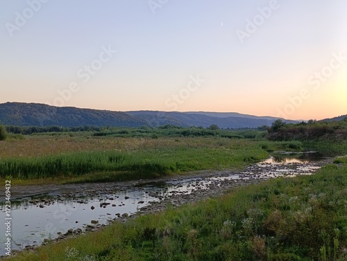 Sunset over a serene river landscape with rolling hills and lush greenery at twilight