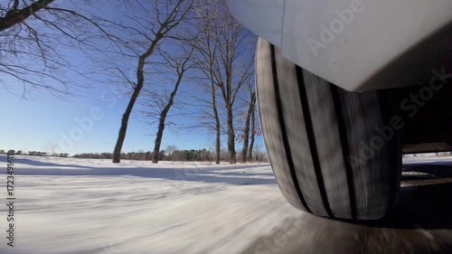 Close-up of a tire on a fast-moving car on a snowy road. Close-up of a gray car wheel moving fast on a snowy country road surrounded by a forest on a sunny winter day