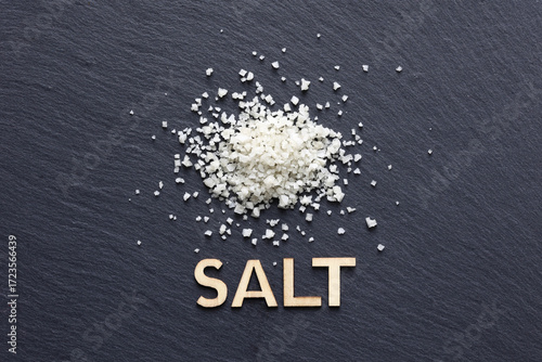 Dried coarse salt on black slate background with wooden word Salt