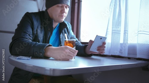 Leisurely Train Ride: Man Sips Tea, Connects on a Video Call, and Soaks in the Scenic Landscape Outside