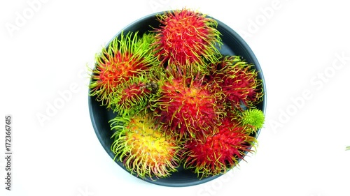 Top view rotation of ripe sweet rabutan fruits in black ceramic dish on white background.