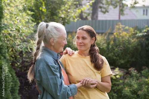 an elderly woman hugs her adult daughter near the house in the garden. Deep conversation. emotional intimacy. support in two age generations