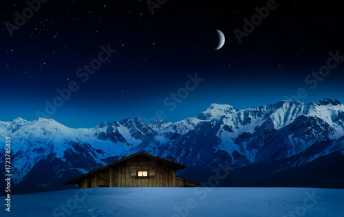 Berghütte  mit beleuchtetem Fenster vor einer verschneiten Bergwelt