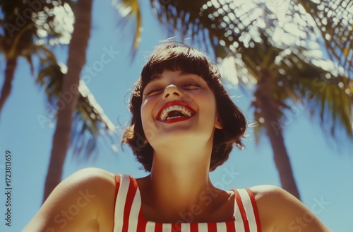Woman Smiling Joyfully in a Striped Outfit Under Palm Trees During a Sunny Day