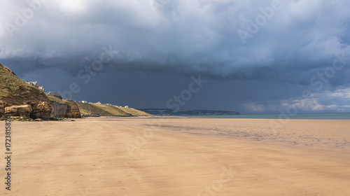 A seaside scene of a sunny beach with dark clouds forming in the distance.