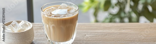 A refreshing iced coffee drink served in a glass with ice cubes, accompanied by a small bowl of additional ice, set against a natural backdrop.